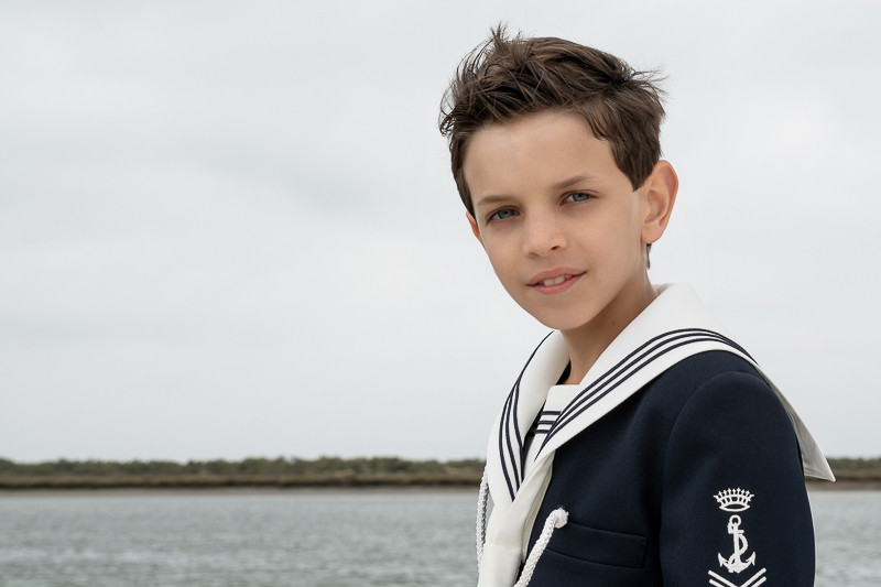 Fotografía de niño vestido de marinero para su primera comunión sobre un fondo natural de mar y costa