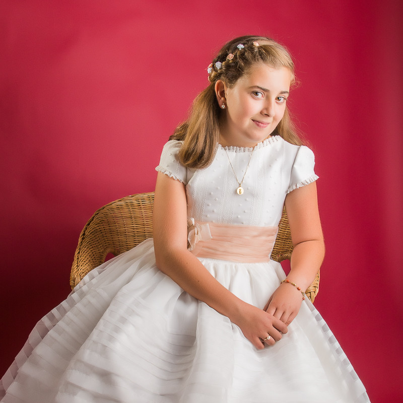 Fotografía de niña vestida para su primera comunión sobre un fondo burdeos en estudio